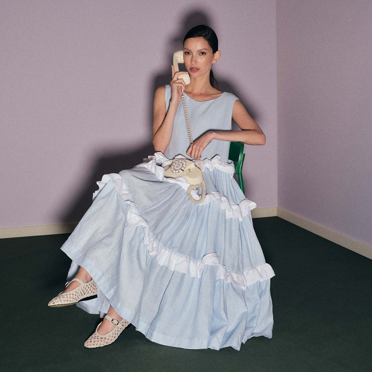 Model wearing Kindred Of Ireland sleeveless maxi dress with frilly detail, sitting holding a vintage phone to the ear.