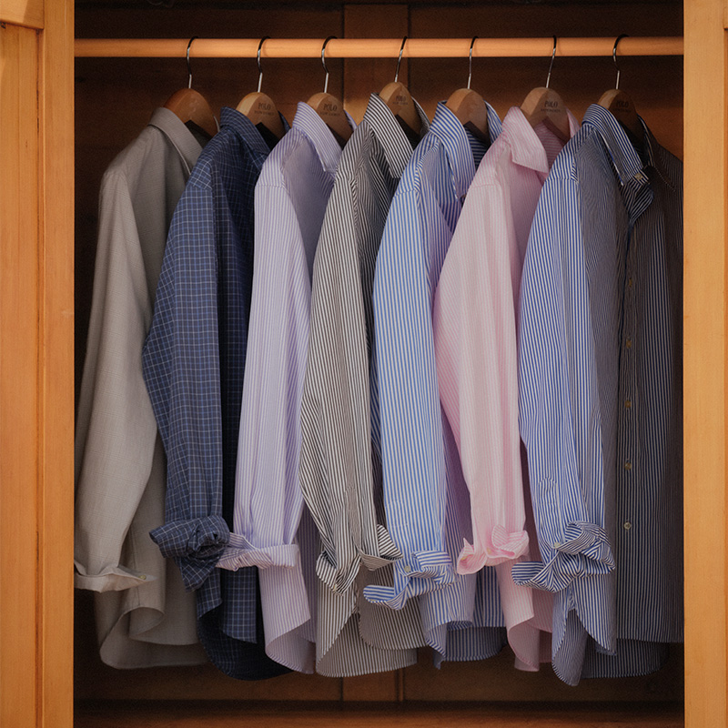 A row of neatly hung long-sleeve shirts in various colors and patterns inside a wooden closet.