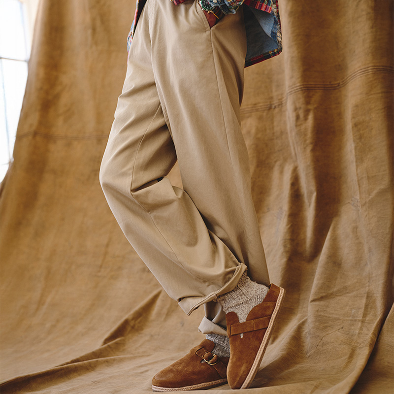Person in beige pants and brown shoes with patterned socks, posing against a brown fabric backdrop.