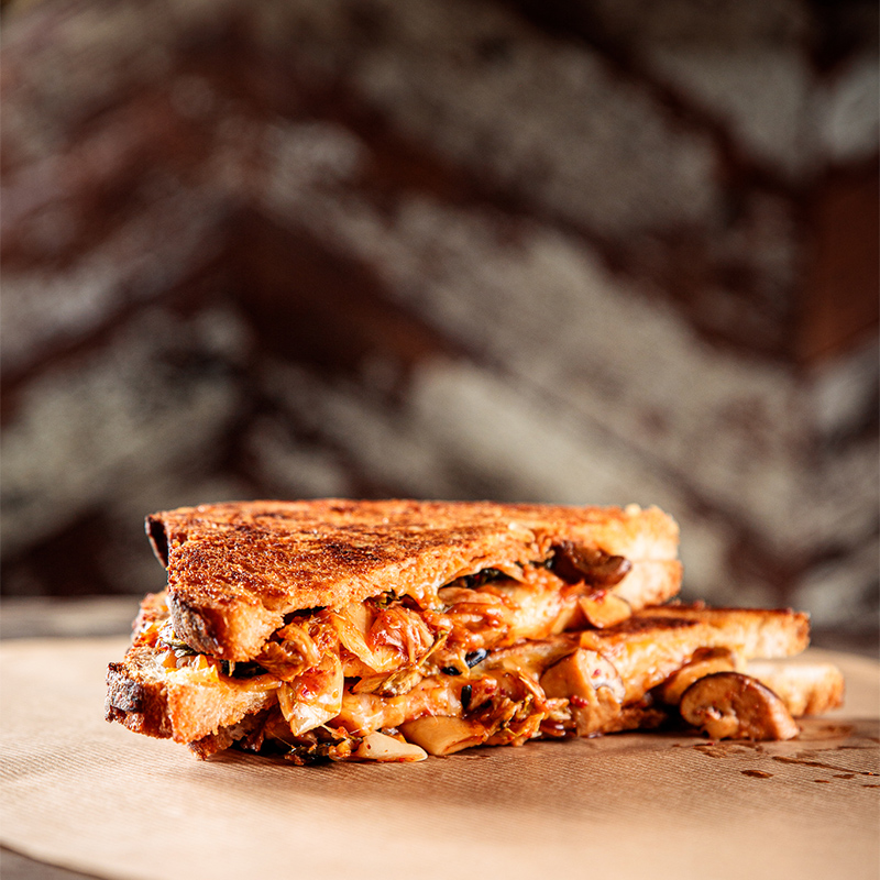 A grilled cheese sandwich with fillings, sliced in half, placed on a surface.
