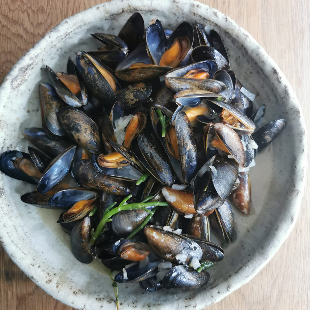 A bowl of cooked mussels with herbs on a wooden table.
