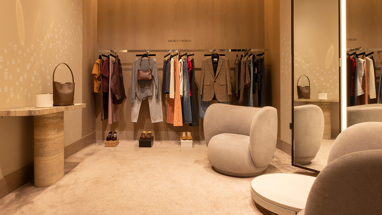 Chic clothing store fitting room with racks, modern chairs, and full-length mirror.
