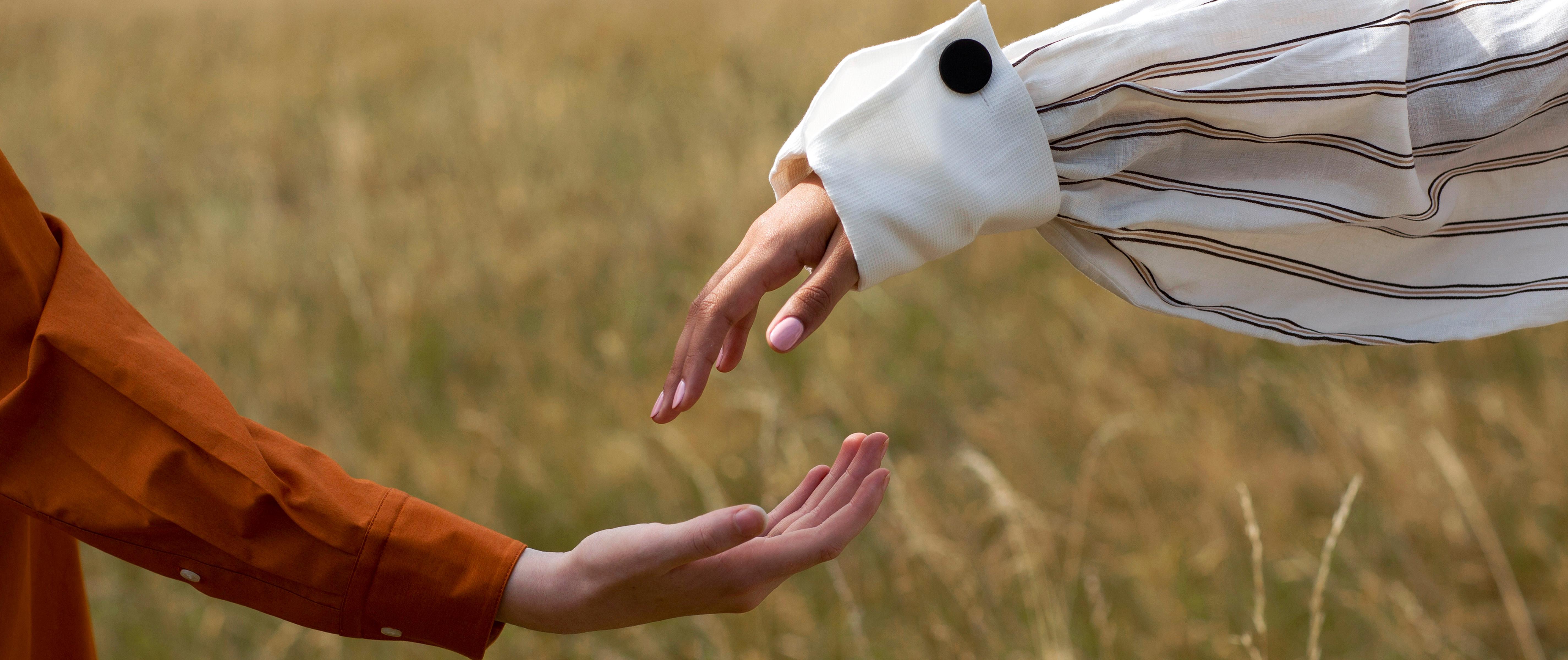 Two people holding hands against a blue sky with clouds.