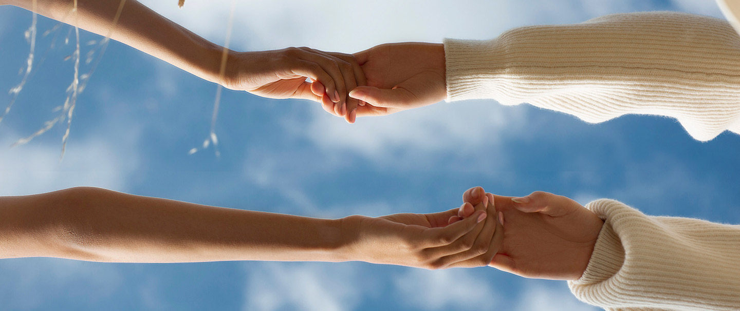 Two people holding hands against a blue sky with clouds.