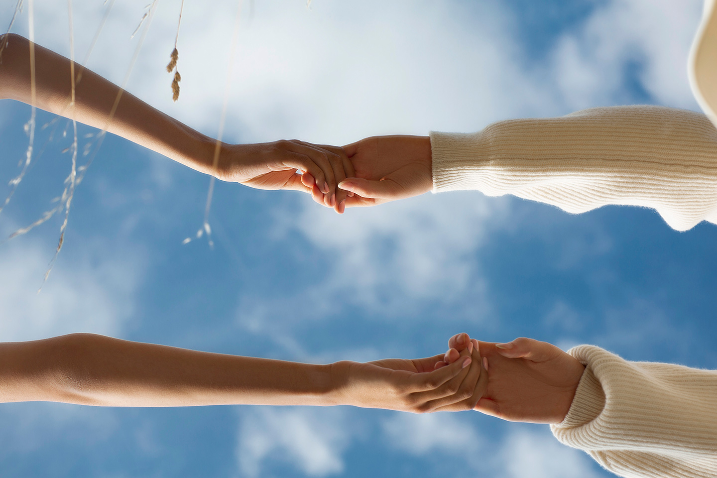 Two people holding hands against a blue sky with clouds.