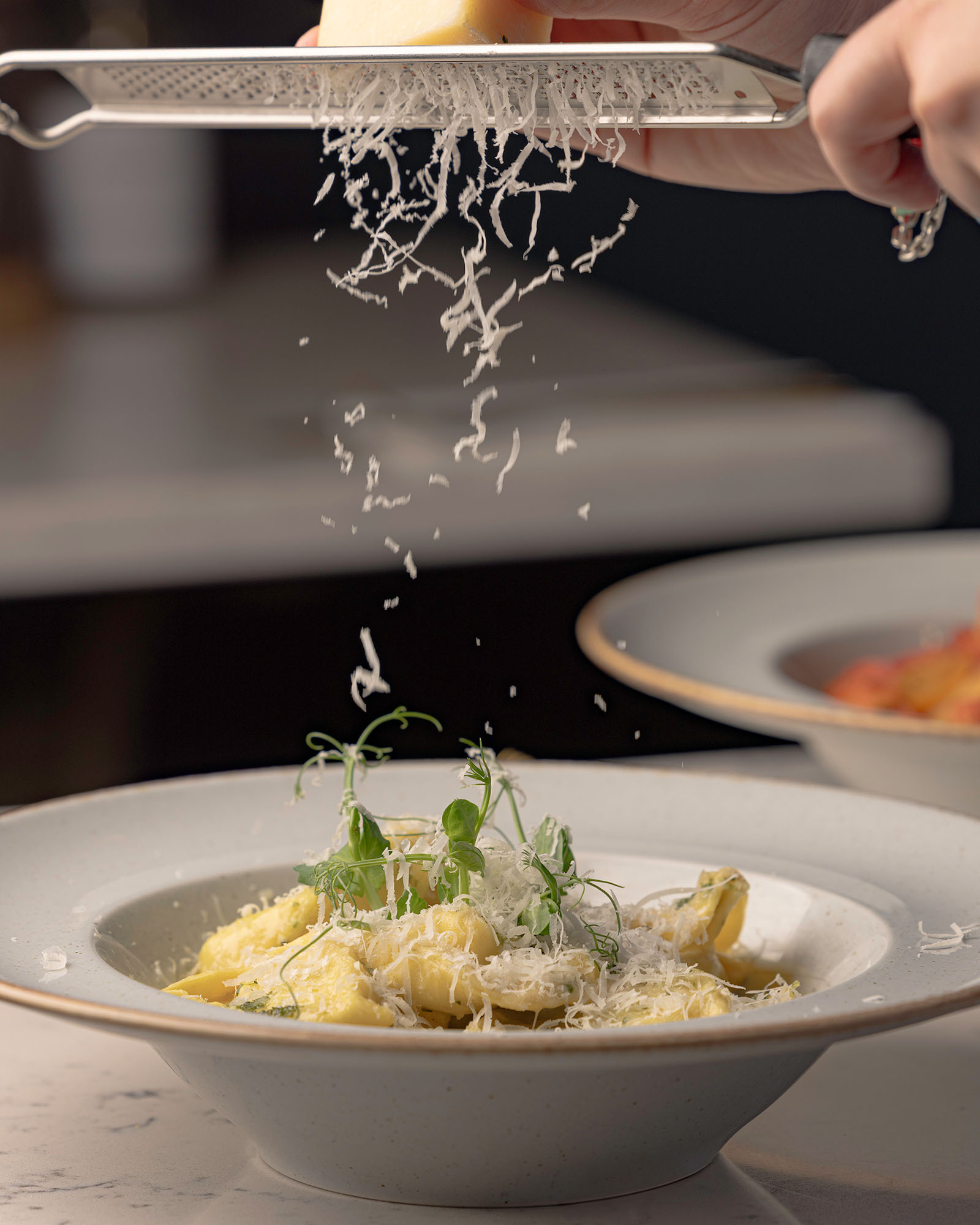Close up photo of Chef grating cheese onto pasta dish